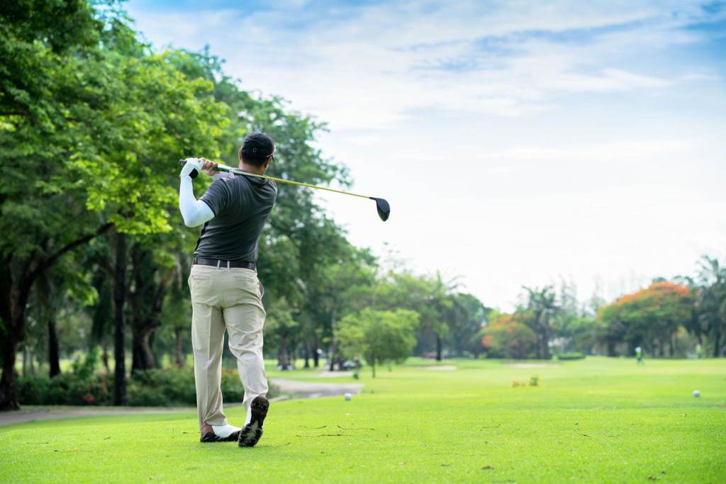 Golfer hitting golf shot with club on course while on summer vacation
