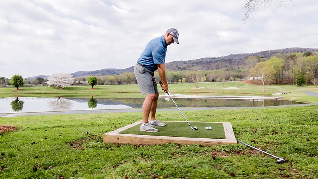 Golf practice mat on backyard grass with golfer hitting a ball using a driver.