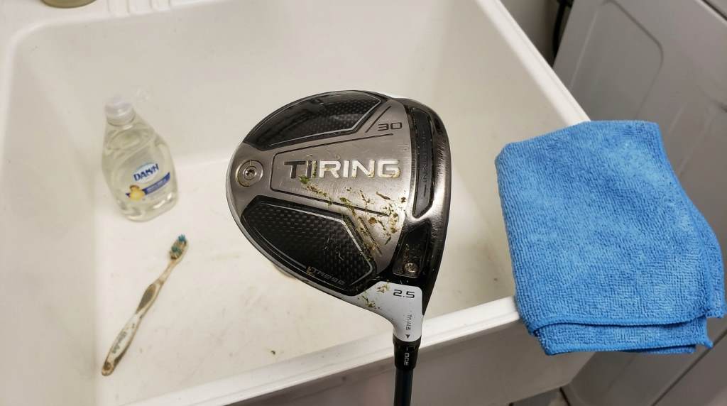 Golfer cleaning a golf driver with a microfiber cloth at home